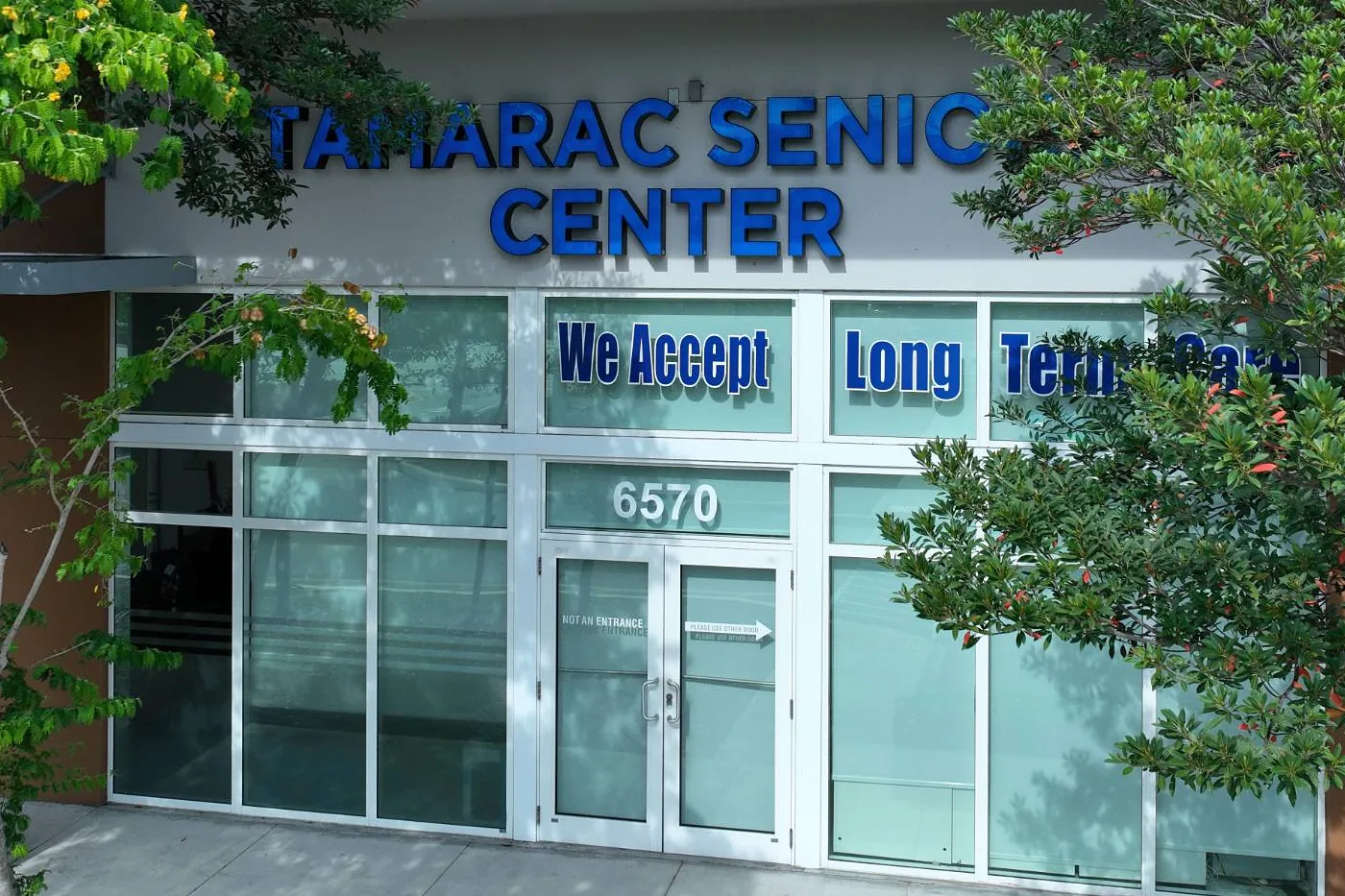 Vista aérea de la entrada de Tamarac Senior Center en 6570 N University Dr, con el letrero azul del centro sobre la puerta y árboles a ambos lados